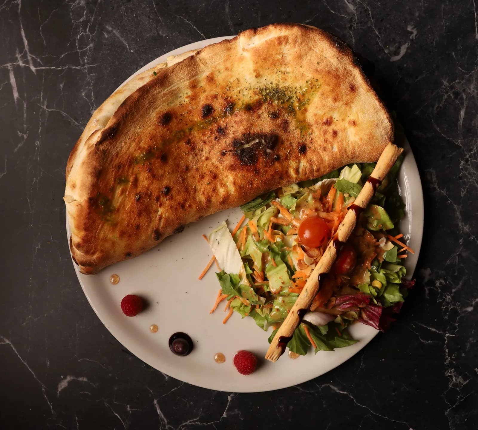 Calzone dorée servie avec une salade fraîche, tomates cerises et gressin