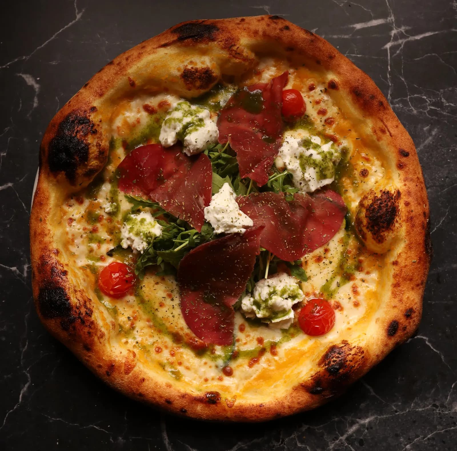 Pizza au feu de bois, bresaola, burrata, roquette, tomates cerises et pesto